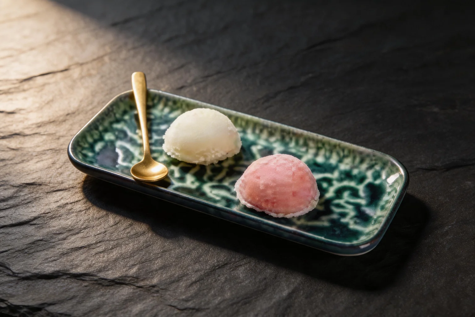 Mochi glacé on a long patterned green dish with a gold spoon, dark slate background
