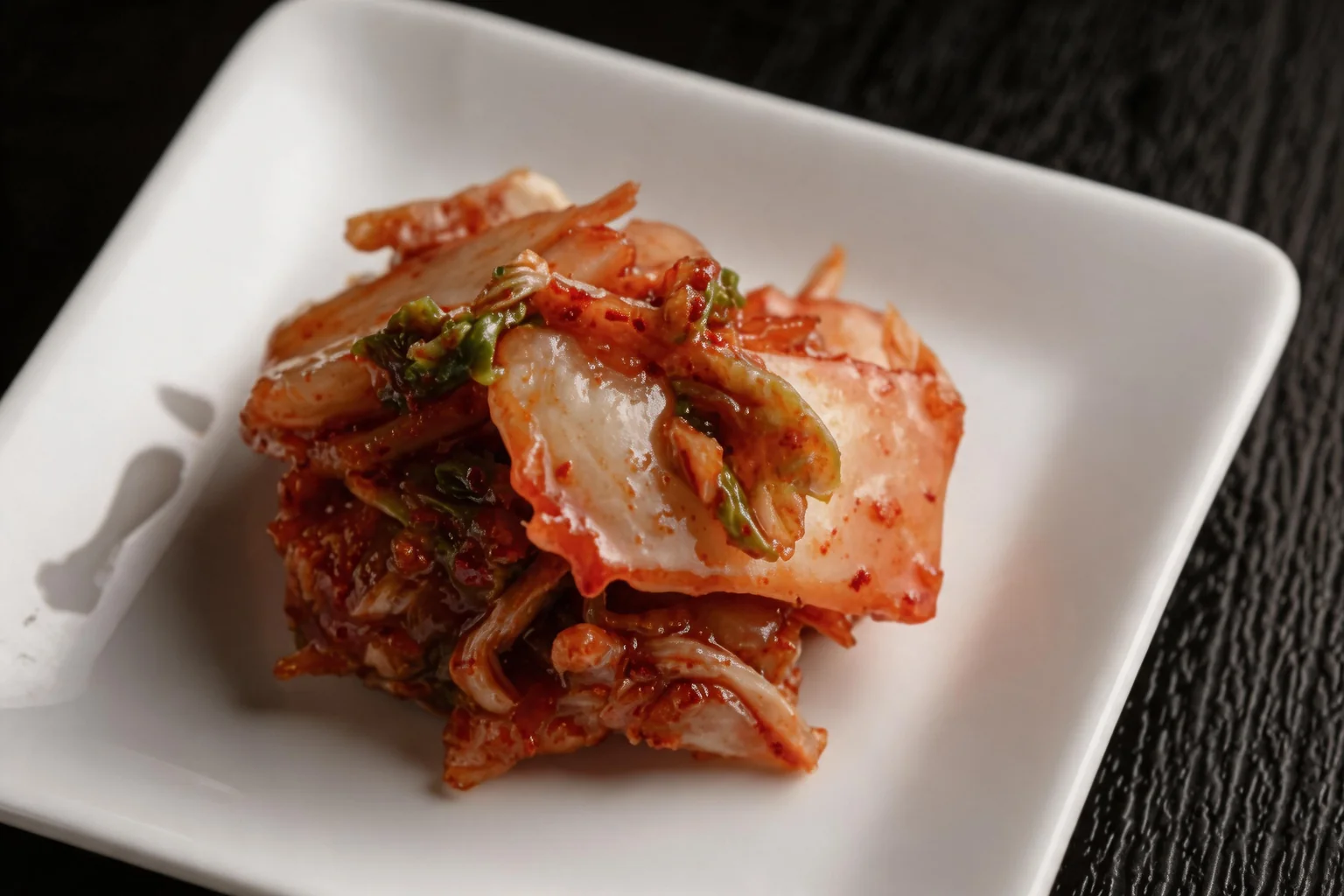 Kimchi on a white square plate, black wooden table